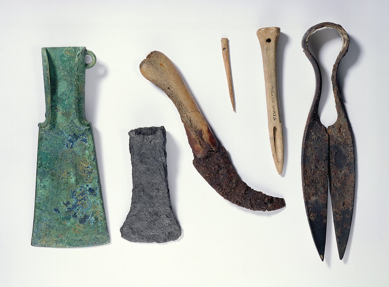 Auswahl an Werkzeugen: L-R: frühe Eisenzeit Bronzeaxt mit umgebogenen Flügeln; spätere Eisenaxt; Messer mit einem Knochenheft; Knochennadel; Knochenpfriem; Eisenschere von Iron Age