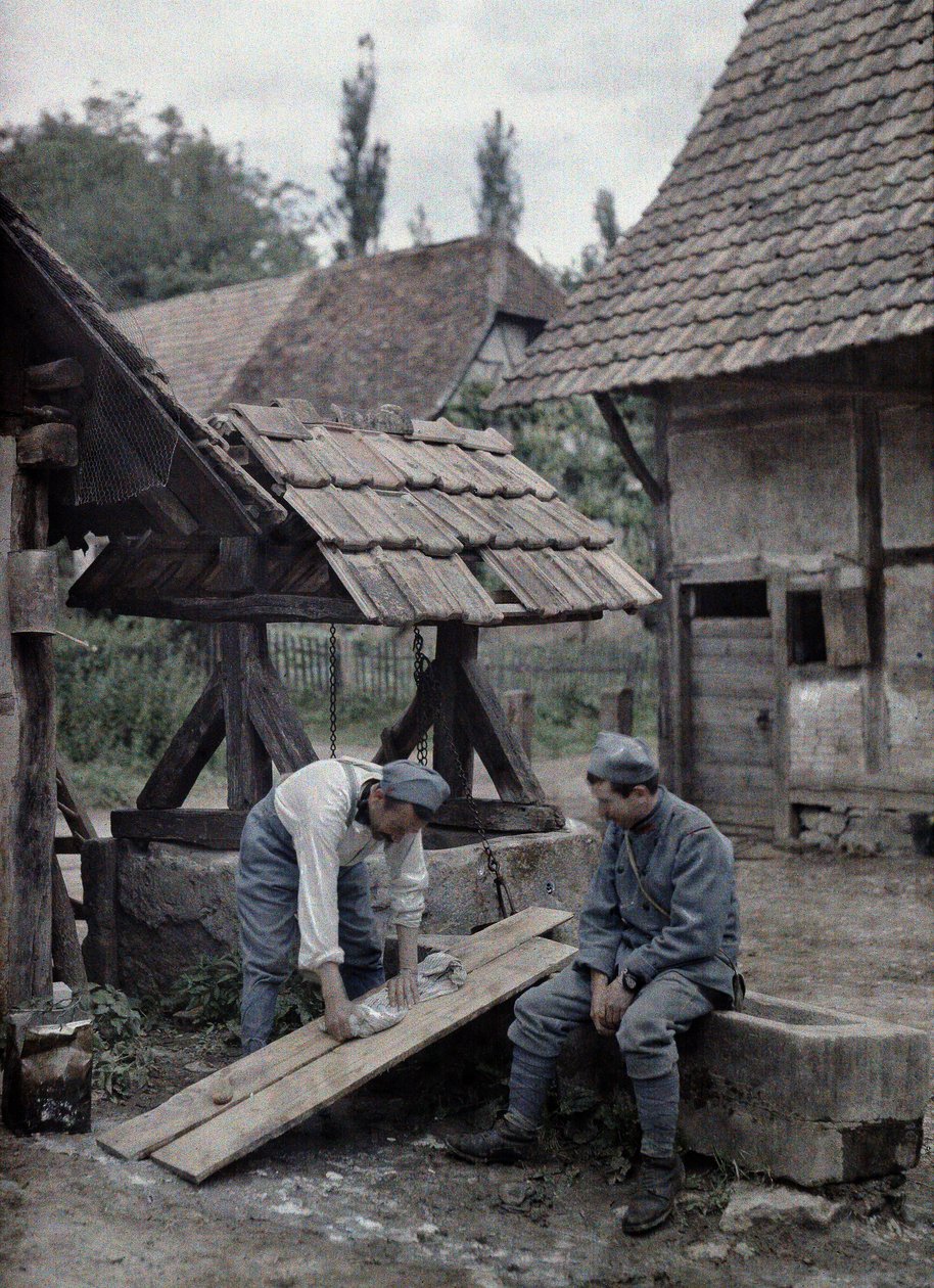 Zwei französische Soldaten kümmern sich um ihre Wäsche, indem sie Bretter auf den Trog eines Brunnens nahe einem Bauernhaus in der Stadt Gildwiller, Département Haut-Rhin, Elsass, Frankreich, 21. Juni 1917 von Paul Castelnau