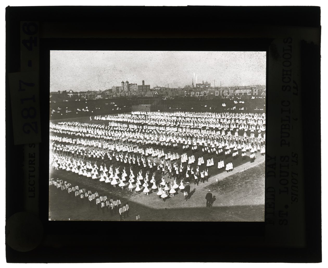 Horizontales, schwarz-weißes Foto von Hunderten von Schulkindern, die für die Feldtagparade und das Fest in Formation stehen. Alle Mädchen in weißen Kleidern und die Jungen in weißen Hemden und Krawatten mit dunklen Hosen von Unbekannt Unbekannt